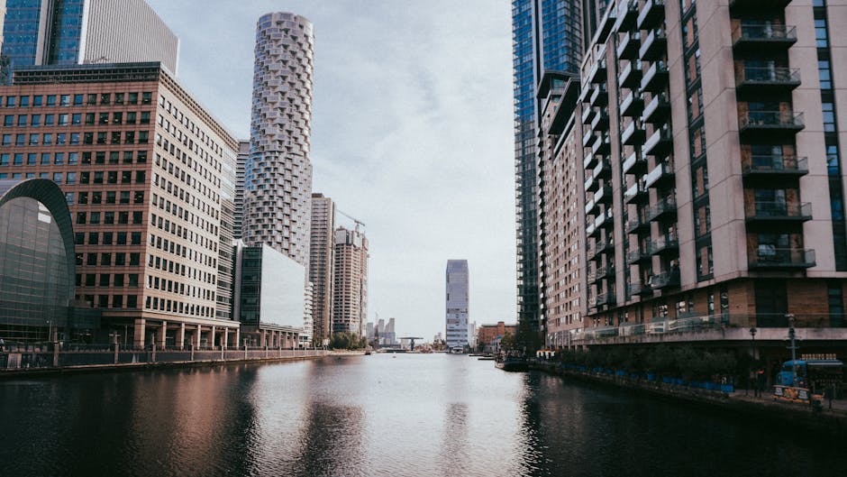 A panoramic view of South Quay Canary Wharf E14 during sunset, showcasing a modern skyline with high-rise buildings constructed from glass and steel, reflecting the warm hues of the setting sun. The b